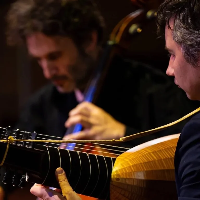 A man plays a cello as another man accompanies him on a lute.
